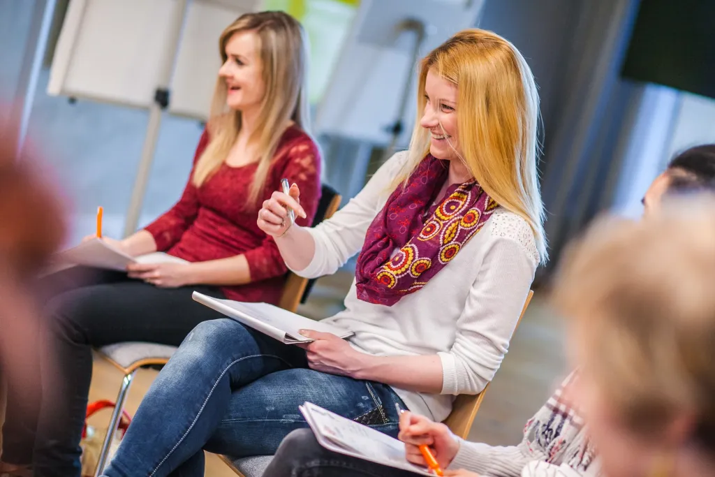 Teilnehmerinnen eines Workshops lachen und machen Notizen